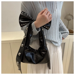 Detail of black patent leather bag with oversized bow and silver studded rivets