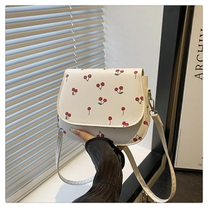 Close-up of a white saddle bag with red cherry print and silver metallic buckle detail