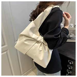 Detail of minimalist cream shoulder bag with large bow design and matte leather finish