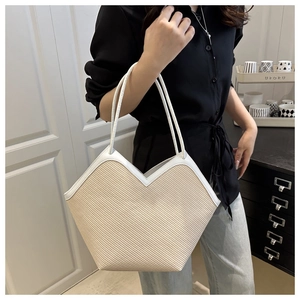 Detail of beige woven tote bag featuring white leather trim and a unique V-shaped opening
