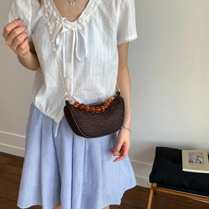 Vintage brown woven saddle bag with amber beads and gold chain strap on white wall