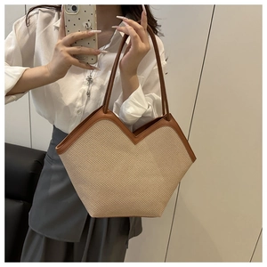 Detail of a woven beige tote bag with brown leather handles held by a model in a mirror