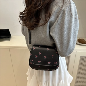 Black leather saddle bag with cherry print and adjustable strap shown on model