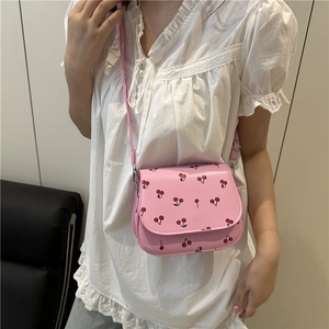 Pink saddle bag with cherry print and adjustable strap shown on a model