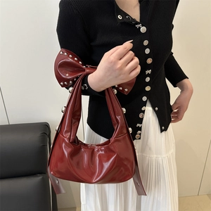 Sac bandoulière en cuir verni rouge avec grand nœud et clous porté par un mannequin