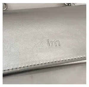 Détails de la texture plissée argentée et logo mim embossé sur le petit sac à main