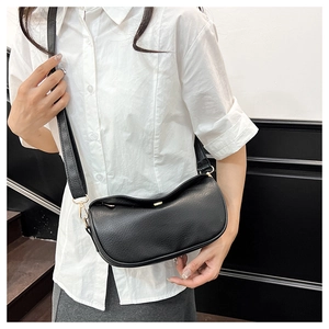 Detail of black pebbled leather crossbody bag featuring gold hardware on female model