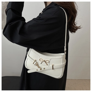 Close-up of a white shoulder bag featuring a golden bow metal piece and textured leather