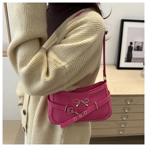 Close-up of pink leather shoulder bag featuring a decorative golden metal bow detail