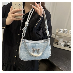 Detail of glittery blue denim underarm bag with silver bow and pearl chain charm
