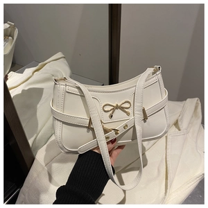 Detail of creamy white underarm bag with elegant golden bow clasp and thin shoulder strap