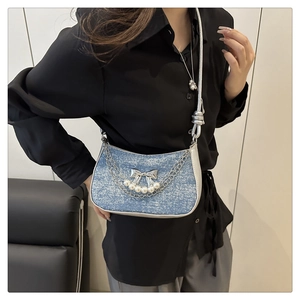 Detail of blue denim hobo bag featuring silver bow, pearl tassel and metal chain strap