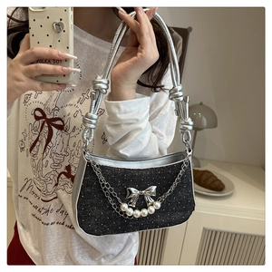 Detail of glittery black underarm bag featuring silver bow and pearl chain decor