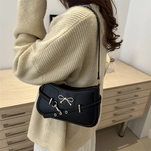 Classic black leather underarm shoulder bag with a gold bow buckle worn by a model