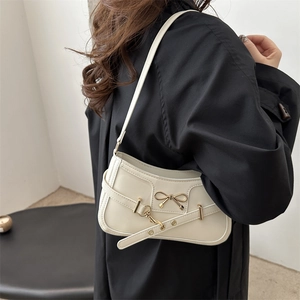 Chic beige underarm bag with gold bow ornament worn by a model in a minimal setting