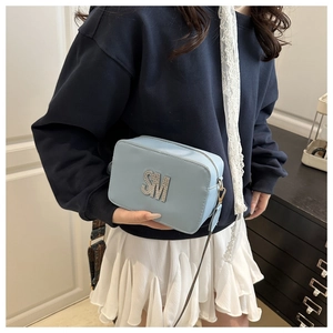 Close-up of light blue leather crossbody bag with SM metal logo and wide patterned strap
