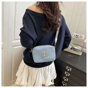 Detail of light blue crossbody bag featuring a large rhinestone SM logo and wide woven strap