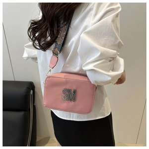 Detailed shot of pink textured crossbody bag with rhinestone logo and woven strap