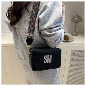 Detail of black crossbody bag with rhinestone SM logo and colorful woven guitar strap