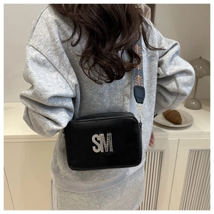 Detail of black crossbody bag with rhinestone SM letters and ethnic woven wide strap