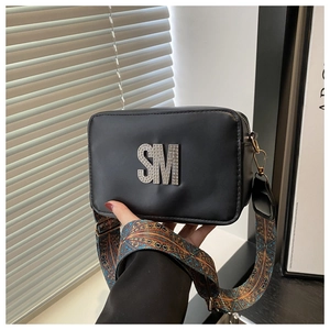 Detail of black crossbody bag with rhinestone SM logo and wide patterned fabric strap