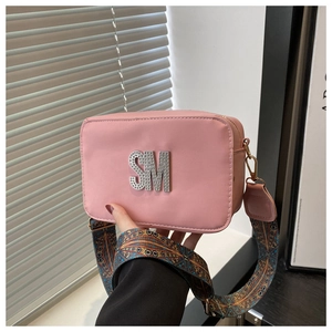 Detail of pink leather crossbody bag featuring diamond SM logo and geometric wide strap