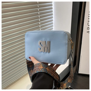 Detail of light blue square camera bag featuring rhinestone SM logo and wide woven strap