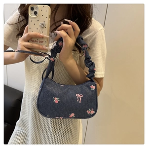 Detail of denim underarm bag with pink bow print and ruffled cloud shoulder strap
