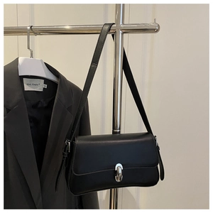 Detail of black leather underarm bag with a round silver metallic lock displayed on a stand