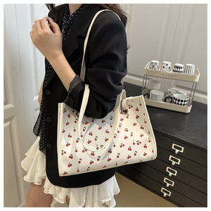 Close-up of white tote bag with red cherry prints and slim shoulder straps on a cabinet