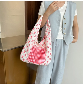 Détail du sac cabas en toile avec nœuds rouges et poche à carreaux avec ruban blanc