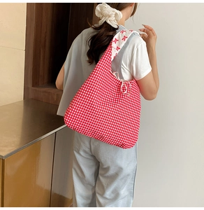 Détail du tote bag en toile vichy rouge avec bandoulière fleurie porté par mannequin