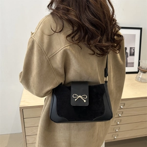 Minimalist black crossbody bag with gold bow on a model in a cozy interior setting