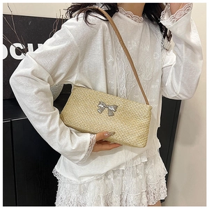 Detail of a beige woven straw bag featuring a silver metal bow buckle and brown strap