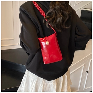 Close-up of mini red glossy crossbody bag featuring pearl accent and braided strap