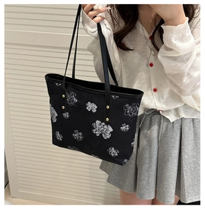 Détail d'un sac cabas noir avec motifs floraux blancs et rivets métalliques dorés