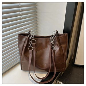 Detail of dark brown tote bag featuring geometric textured stitching and silver metal chain