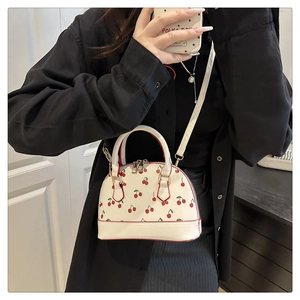 Détail du sac coquille blanc à imprimé cerise avec bords rouges et finitions dorées