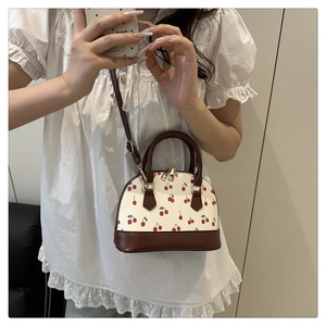 Detail of cute white shoulder bag with cherry print and brown leather handles and straps