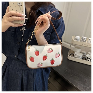 Detail showing white strawberry print square crossbody bag with brown trim and gold chain