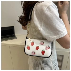 Detail of white strawberry print shoulder bag with gold chain strap on female model