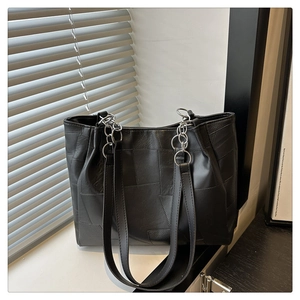 Detail of black patchwork tote bag with silver chain straps on a minimalist windowsill