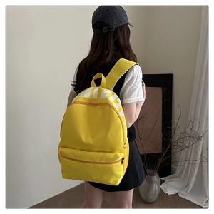 Side view of a bright yellow canvas backpack worn by a model in a cozy home setting