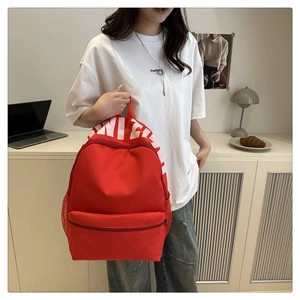 Detail of red travel backpack featuring white lettering, front pocket, and side mesh bag