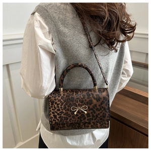 Detail of leopard print crossbody bag with gold bow clasp on casual knit outfit