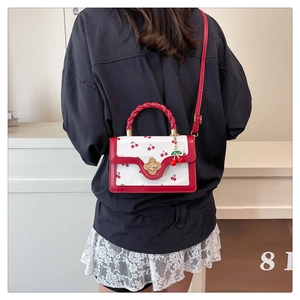 Detail of red cherry print square bag with twisted handle and floral gold buckle