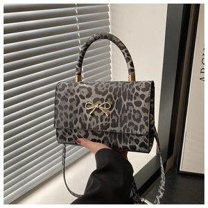 Detail of grey leopard print handbag featuring a gold metal bow and cylindrical handle