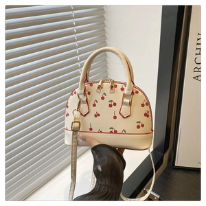 Detail of white shell crossbody bag featuring red cherry print and golden double zippers