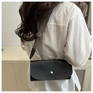 Detail of black crocodile pattern crossbody bag with wide woven strap and gold buckle