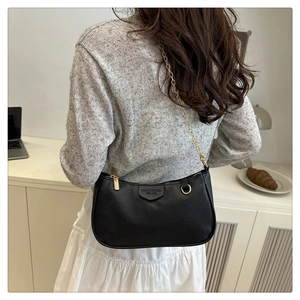 Close-up of black litchi grain leather bag featuring gold chain strap and hardware details